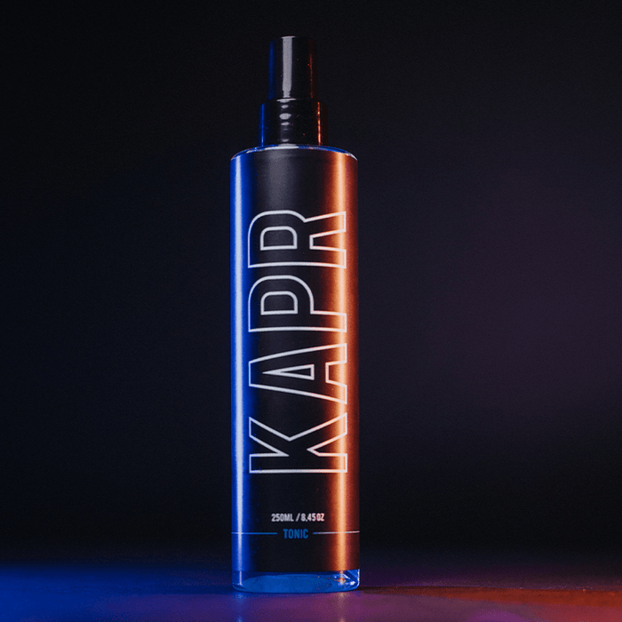 KAPR Tonic – zwarte fles met oranje-blauwe gloed, modern barbershop design.