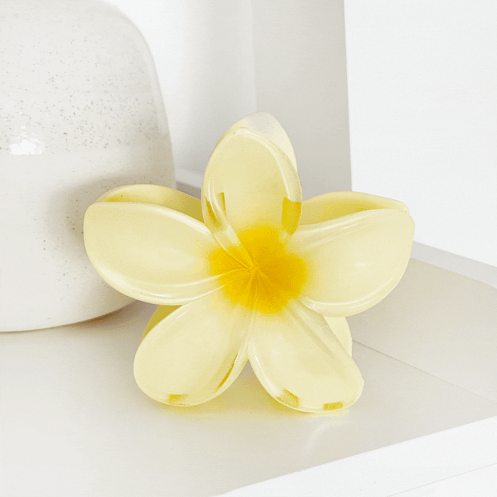 Golden yellow tropical flower claw clips from Coconut Lane on a white shelf beside a ceramic vase.