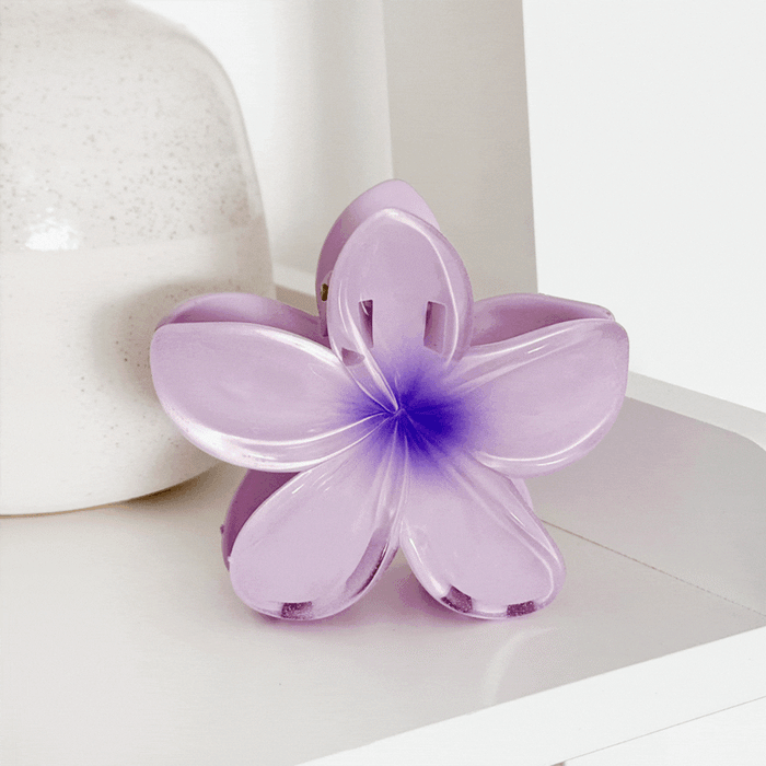 Tropical flower-patterned claw clips in vibrant colors on a white shelf next to a simple ceramic vase.
