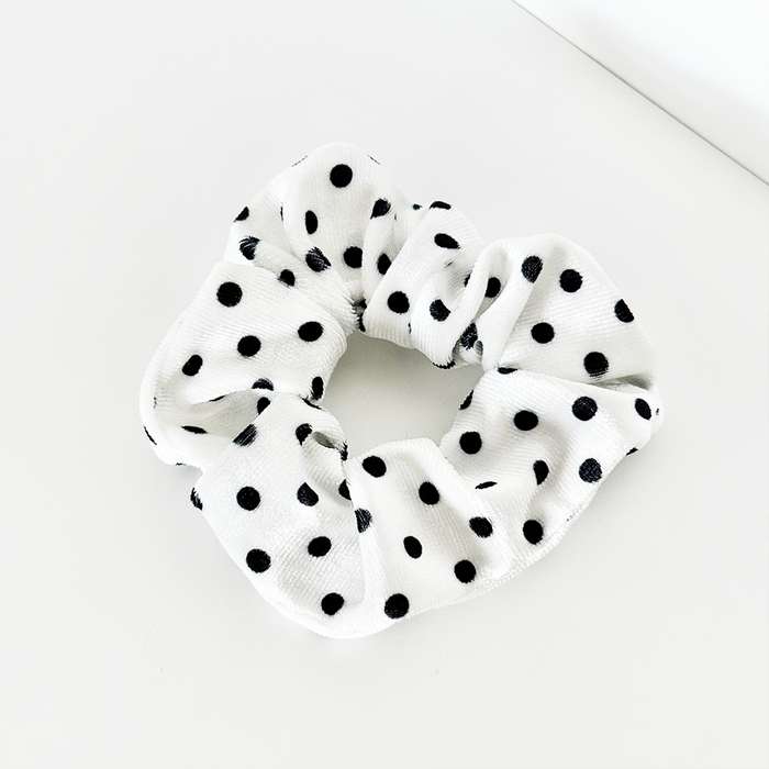 White scrunchie with black polka dots on soft fabric.