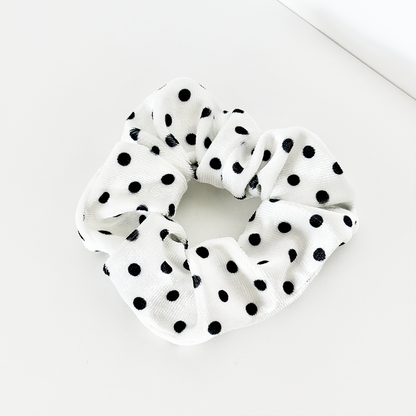 White scrunchie with black polka dots on soft fabric.