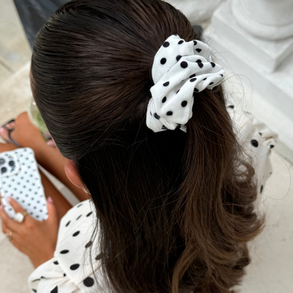 Woman with brown hair wears a white polka dot scrunchie and matching shirt, holding a polka dot phone case.
