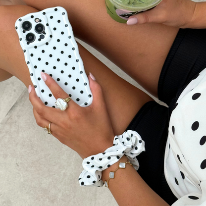 Woman with a drink and phone, wearing a white polka dot scrunchie in her hair.